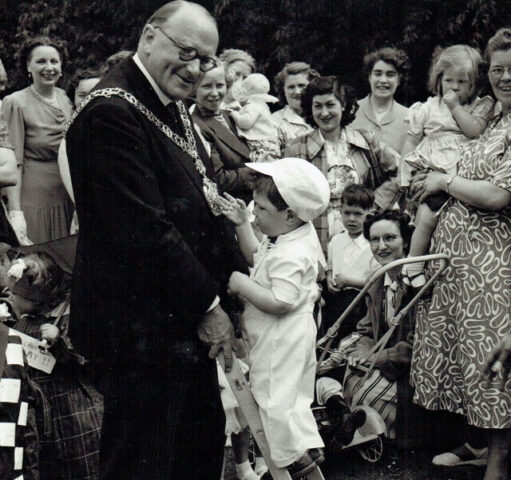 Alderman W J Grimshaw lets a small child look at this Mayoral Regalia. 